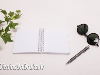 Atvērta piezīmju grāmata ar spirāles iesiešanu, pildspalvu un saulesbrillēm